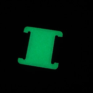 Könnte beinhalten: Eine grüne, im Dunkeln leuchtende Kunststoffschnalle mit zwei Löchern.