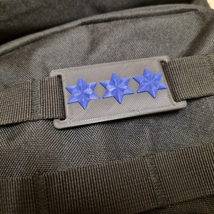 Könnte beinhalten: Eine schwarze Stofftasche mit einem blauen Sternen-Patch. Der Patch hat drei blaue Sterne auf grauem Hintergrund.