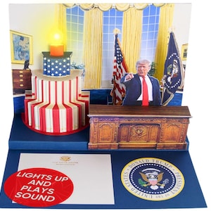 May include: A pop-up card depicting the Oval Office with a desk, American flags, and a figure of Donald Trump. The card lights up and plays sound. The text "Lights Up and Plays Sound" is printed on the front of the card.