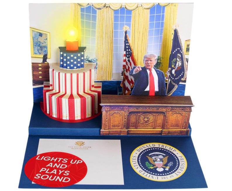 May include: A pop-up card depicting the Oval Office with a desk, American flags, and a figure of Donald Trump. The card lights up and plays sound. The text "Lights Up and Plays Sound" is printed on the front of the card.