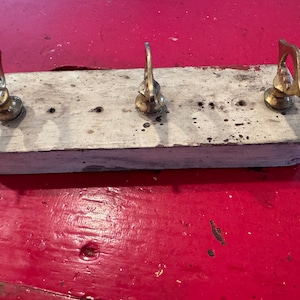 Peut inclure: Une étagère en bois rustique avec trois crochets dorés. L'étagère est peinte en blanc et a un aspect vieilli. Les crochets sont décoratifs et ont un design unique.