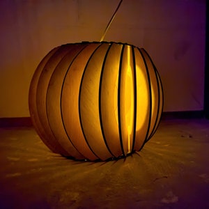 May include: A wooden lampshade in the shape of a sphere with a geometric design. The lampshade is lit from within, casting a warm glow.