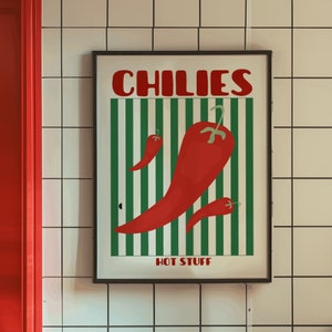 May include: A black framed poster with the word "CHILIES" in red letters and a green and white striped background. The poster features a red chili pepper with the text "HOT STUFF" at the bottom.