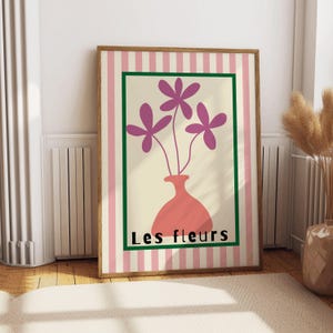 May include: A pink and green striped poster with a vase of purple flowers. The vase is a light orange color and the text "Les fleurs" is printed below the vase.