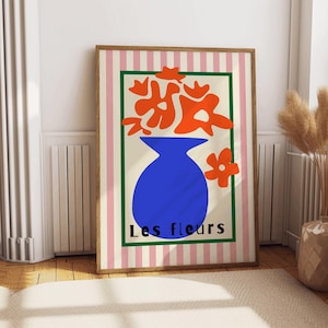 May include: A framed print with a pink and white striped background. The print features a blue vase with orange flowers and the text "Les fleurs".