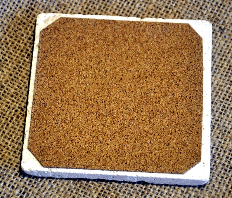 May include: A square cork coaster with a white border. The coaster is made of natural cork and has a slightly rough texture.