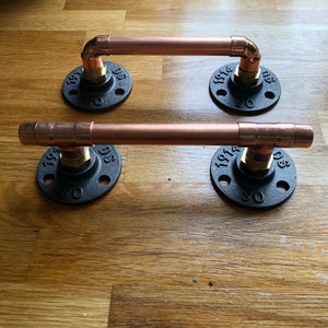 May include: Two copper pipe door handles with black iron flanges. Each flange has the numbers "1914" and "D3" and the text "SO".