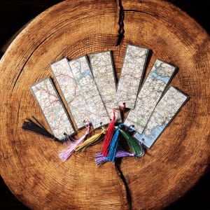 Könnte beinhalten: Sechs rechteckige Lesezeichen mit detaillierten Vintage-Kartenmotiven, die verschiedene Topografien und Straßennetze zeigen. Jedes Lesezeichen ist mit einer farblich unterschiedlichen Quaste in Schwarz, Pink, Gelb, Rot, Blau, Grün oder Violett versehen.