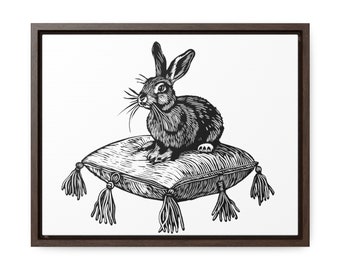 May include: Monochrome illustration of a rabbit seated on a cushion with tassels, presented in a dark brown wooden frame. The rabbit features long ears and whiskers. The artwork is in black and white.