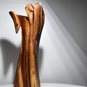 Puede incluir: Una escultura de madera abstracta con una forma natural y orgánica. La escultura está hecha de madera con diferentes tonos de marrón y beige, y presenta un acabado liso y pulido. El diseño tiene una forma única y fluida.