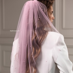 Op de afbeelding: Een lichtroze bruidssluier met parelaccenten. De sluier wordt over een witte blazer gedragen. De tekst "MyBridalLook" is zichtbaar. Een bruiloftsaccessoire.