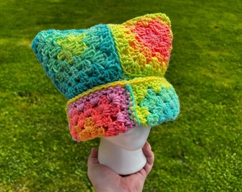 May include: A colorful crocheted hat with a rainbow pattern. The hat is made of yarn in shades of pink, green, yellow, and blue.