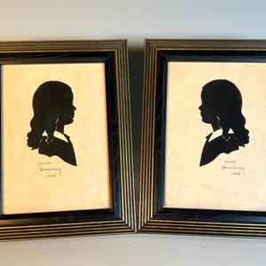 May include: Two framed silhouette portraits of a person in profile, with dark hair and a collared shirt. The frames are black with gold trim. Each portrait has the name "Jennie Browning" and the year "1945" written below the silhouette.