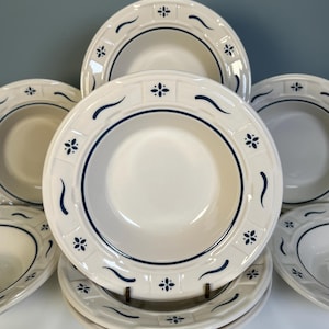 May include: A set of off-white ceramic bowls with a blue floral and wave design. The bowls have a wide rim with a repeating pattern of small blue flowers and curved lines. The bowls are stacked and arranged on a white surface.