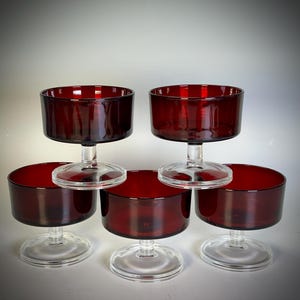 May include: Six stemmed glasses with a deep red bowl and clear stem and base. The glasses are arranged in a pyramid shape, with one glass on top, two in the middle, and three on the bottom. The glasses are empty and appear to be made of glass.