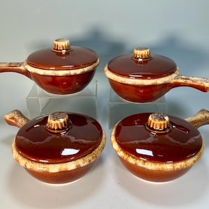 May include: A set of four round ceramic soup bowls with matching lids and side handles. Each bowl features a glossy dark brown glaze on the top and lid, transitioning to a textured, lighter cream-colored drip pattern around the rim and handle.