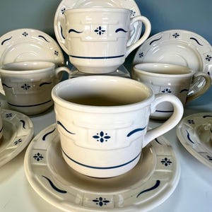 May include: Cream-colored ceramic teacups and saucers set. The cups and saucers feature a blue floral and wave design. The cups have a handle and are sitting on matching saucers. The set is perfect for serving tea or coffee.