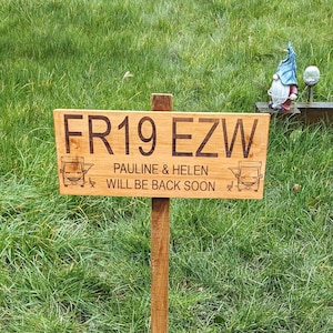May include: A wooden sign with the text "FR19 EZW Pauline & Helen will be back soon" on a green grassy lawn. The sign is attached to a wooden stake.