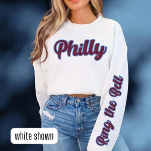May include: White sweatshirt with the word "Philly" in maroon with a blue outline on the front and the phrase "Ring the Bell" in blue on the right sleeve.