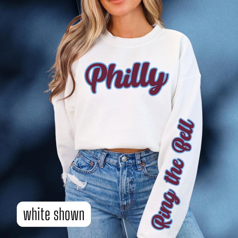 May include: White sweatshirt with the word "Philly" in maroon with a blue outline on the front and the phrase "Ring the Bell" in blue on the right sleeve.