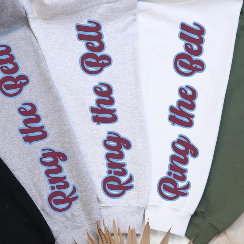 May include: Three sweatshirts in different colors with the text "Ring the Bell" printed on the sleeves. The text is in a maroon color with a light blue outline.