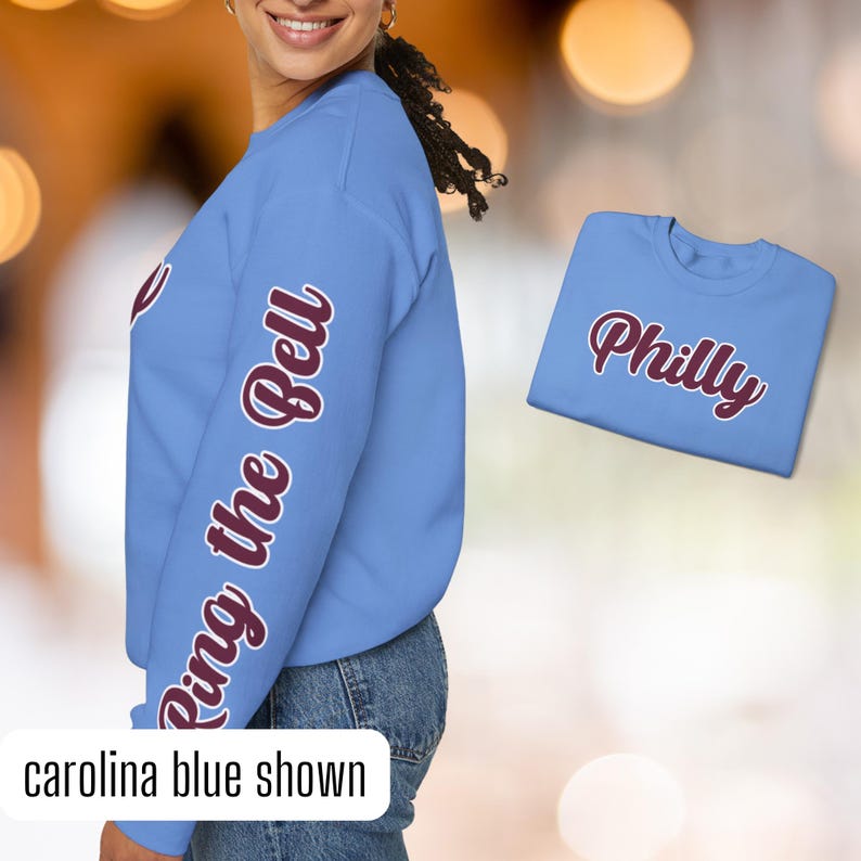 May include: A light blue sweatshirt with the phrase "Ring the Bell" printed in maroon on the left sleeve. The sweatshirt is shown on a model. A separate light blue t-shirt with the word "Philly" printed in maroon is also shown.