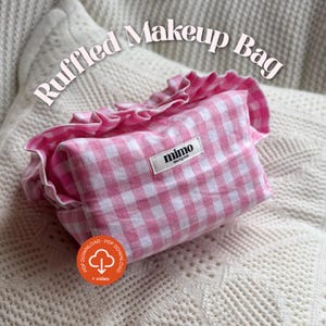 May include: A pink and white gingham makeup bag with a frilled edge. The bag is rectangular and has a small white label reading "mimo sewing club". The words "Ruffled Makeup Bag" are arched above the bag.