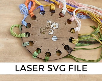 Peut inclure: Organisateur de fils en bois avec 14 trous pour ranger le fil à broder. L'organisateur est décoré d'un motif floral et de trous numérotés. Le fil est enroulé autour de l'organisateur dans un arc-en-ciel de couleurs.