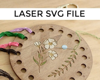 Peut inclure: Un organisateur de fil à broder en bois avec un motif floral et le texte "LASER SVG FILE". L'organisateur comporte plusieurs trous pour tenir le fil et est décoré d'un motif floral et d'une branche feuillue. Diverses couleurs de fil à broder sont visibles.