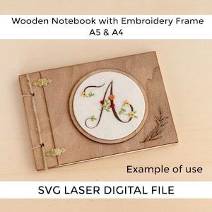 Puede incluir: Un cuaderno de madera con un marco de bordado. El cuaderno presenta un diseño bordado circular con la letra "A" y detalles florales. El cuaderno está encuadernado con herrajes de color latón y cuerda. El texto "Wooden Notebook with Embroidery Frame A5 & A4" es visible.