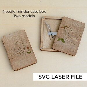 Puede incluir: Caja de madera para agujas con diseño de pájaro. La caja está abierta, revelando agujas en el interior. Se ve el texto "Needle minder case box Two models" y "SVG LASER FILE".