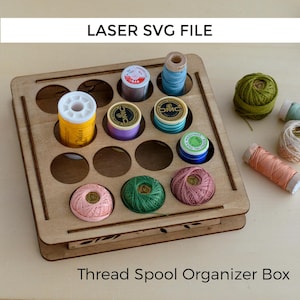 Peut inclure: Une boîte en bois pour organiser les bobines de fil, contenant plusieurs bobines de fil colorées. Les bobines sont de différentes couleurs, dont le jaune, le bleu, le vert, le rose et le violet. Le texte "LASER SVG FILE" et "Thread Spool Organizer Box" sont visibles.
