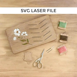 Puede incluir: Tablero de madera con un diseño floral y ranuras para carretes de hilo. El tablero también tiene líneas para marcar las longitudes del hilo. Hay cuatro carretes de hilo de diferentes colores, un par de tijeras y agujas.