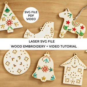 Puede incluir: Seis adornos de madera con agujeros preperforados para bordar. Los adornos tienen forma de árbol de Navidad, pájaro, caballo, campana, círculo y casa. Los adornos están decorados con hilo de bordar de colores. El texto "LASER SVG FILE WOOD EMBROIDERY + VIDEO TUTORIAL" se muestra en una pancarta blanca.