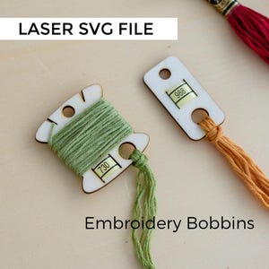 Puede incluir: Bobinas de bordado de madera con hilo verde y naranja. Una bobina está envuelta con hilo verde y etiquetada con el número 730. Otra bobina está etiquetada con el número 988. También se ve el texto "LASER SVG FILE" y "Embroidery Bobbins".