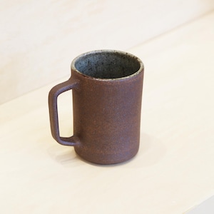 Peut inclure: Une tasse cylindrique en céramique marron avec une anse. La tasse a une surface texturée et un intérieur gris foncé. La tasse mesure environ 10 cm de haut.