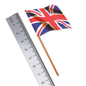 Puede incluir: Una pequeña bandera de la Union Jack en un palo de madera, junto a una regla plateada. La bandera presenta colores rojo, blanco y azul. La regla muestra medidas en centímetros.