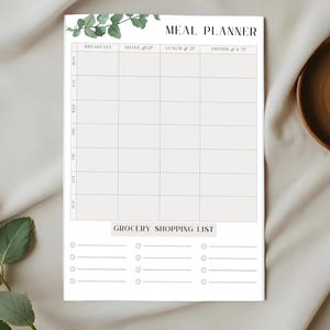 May include: A white meal planner notepad with a weekly layout and a grocery shopping list. The top features a watercolor eucalyptus design. The planner includes sections for breakfast, lunch, dinner, and a shake. The days of the week are listed vertically.