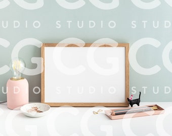 May include: A white framed picture with a light pink lamp and a black cat figurine on a white table with a pink tray and pencils.