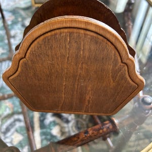 May include: A wooden napkin holder with a scalloped edge design. The holder is made of a medium-toned wood with visible grain, giving it a natural and rustic appearance. The holder is designed to hold napkins and is likely for use on a dining table or countertop.
