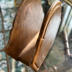 May include: A wooden napkin holder with a scalloped edge design. The holder is made of light brown wood and has a slot to hold napkins. The holder is angled, showing the interior space. The wood grain is visible.