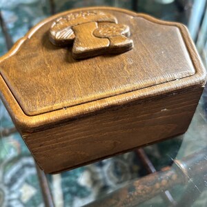 May include: A small, rectangular wooden box with a carved mushroom design on the lid. The box is stained a warm brown color and appears to be vintage. The lid has a curved top edge.