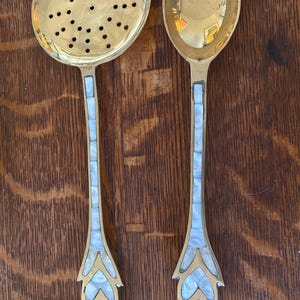May include: A set of two brass serving spoons with mother-of-pearl inlays. The spoons have a decorative design and are perfect for serving food.