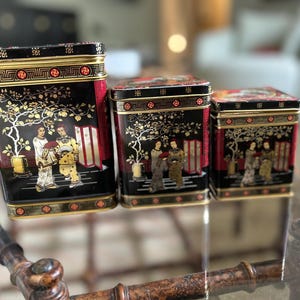 May include: Three black and gold decorative boxes with red accents and Asian-inspired designs. The boxes feature gold trim and intricate patterns.