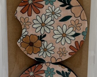 May include: Two round car coasters with a floral pattern of white, orange, and teal flowers on a pink background. The packaging reads "Car Coasters" and "Handmade with love".