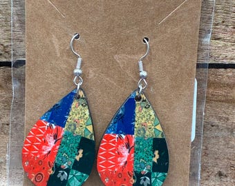May include: A pair of teardrop-shaped earrings with a patchwork design. The earrings feature a mix of red, blue, green, and yellow patterns. The earrings are hanging on silver hooks and are displayed on a brown card.