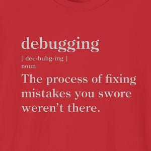 May include: A red t-shirt with the definition of "debugging" printed in white. The definition includes the pronunciation, the word "noun", and the phrase "The process of fixing mistakes you swore weren't there."