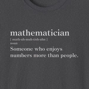 Puede incluir: Una camiseta gris oscuro con texto blanco que dice "matemático [math-uh-muh-tish-uhn] sustantivo Alguien que disfruta más de los números que de las personas."