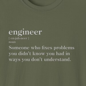 Op de afbeelding: Een groen T-shirt met de definitie van het woord "ingenieur" erop gedrukt in witte tekst. De definitie luidt: "Iemand die problemen oplost waarvan je niet wist dat je ze had, op een manier die je niet begrijpt."