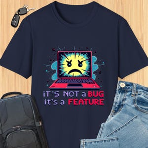 May include: A navy blue t-shirt with a graphic of a laptop screen with a yellow face and a red, white, and blue design. The text "It's not a bug it's a feature" is printed in white below the graphic.